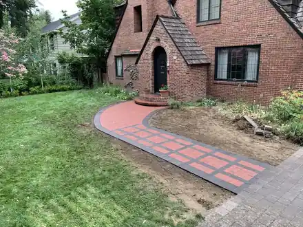 A curved charcoal paver walk with a red brick inlay leading to a brick Tudor house