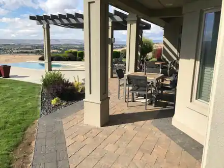 A paver patio under a pergola beside an infinity pool overlooking the Yakima Valley, built by the Roots landscape crew