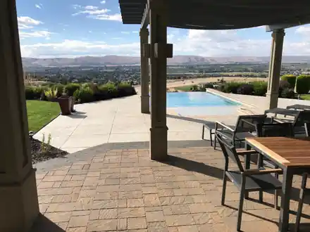 A paver patio under a pergola beside an infinity pool, looking out over the Yakima Valley and its ridgelines