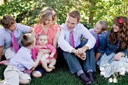 Bryan and Cheryl Johnson sitting on the grass under trees with their five children, in matching pink and lavender