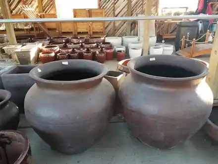 Two wide gray clay urns with flared rims in front of rows of smaller red and cream pots