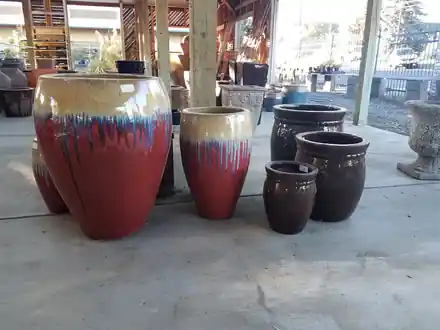 Red drip-glaze ceramic pots grouped under the covered pottery yard at Roots