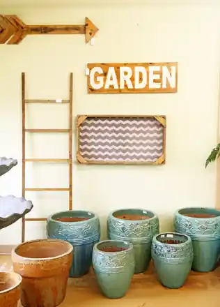 Teal embossed glazed pots and a rusty terracotta pot below a wooden GARDEN sign in the shop