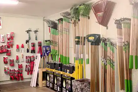 A pegboard wall of rakes, hand pruners and trowels beside boxes of weed barrier fabric in the Roots shop