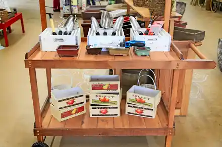 A wooden display cart of garden hand tools and supplies inside the Roots shop